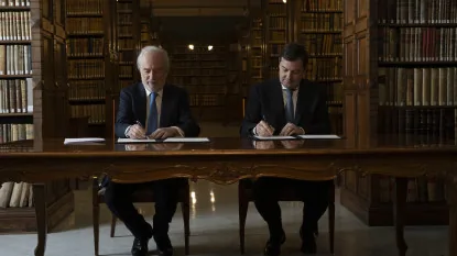 El director de la RAE, Santiago Muñoz Machado, y el presidente de la Junta de Castilla y León, Alfonso Fernández Mañueco, firman en una mesa de madera el acuerdo de adhesión a la Red Panhispánica de Lenguaje Claro y Accesible en la biblioteca de la Academia.