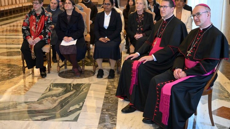 Personas sentadas en una sala del Vaticano durante una audiencia; en primer plano, dos miembros del clero con vestimenta religiosa.